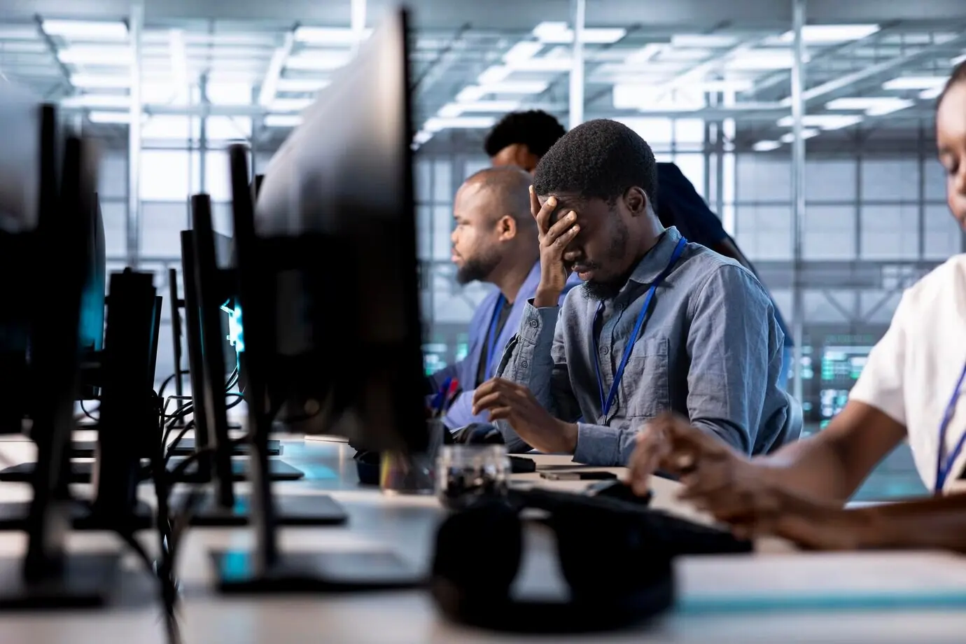 Уставший инженер с головной болью работает в дата-центре, занимаясь его обеспечением.