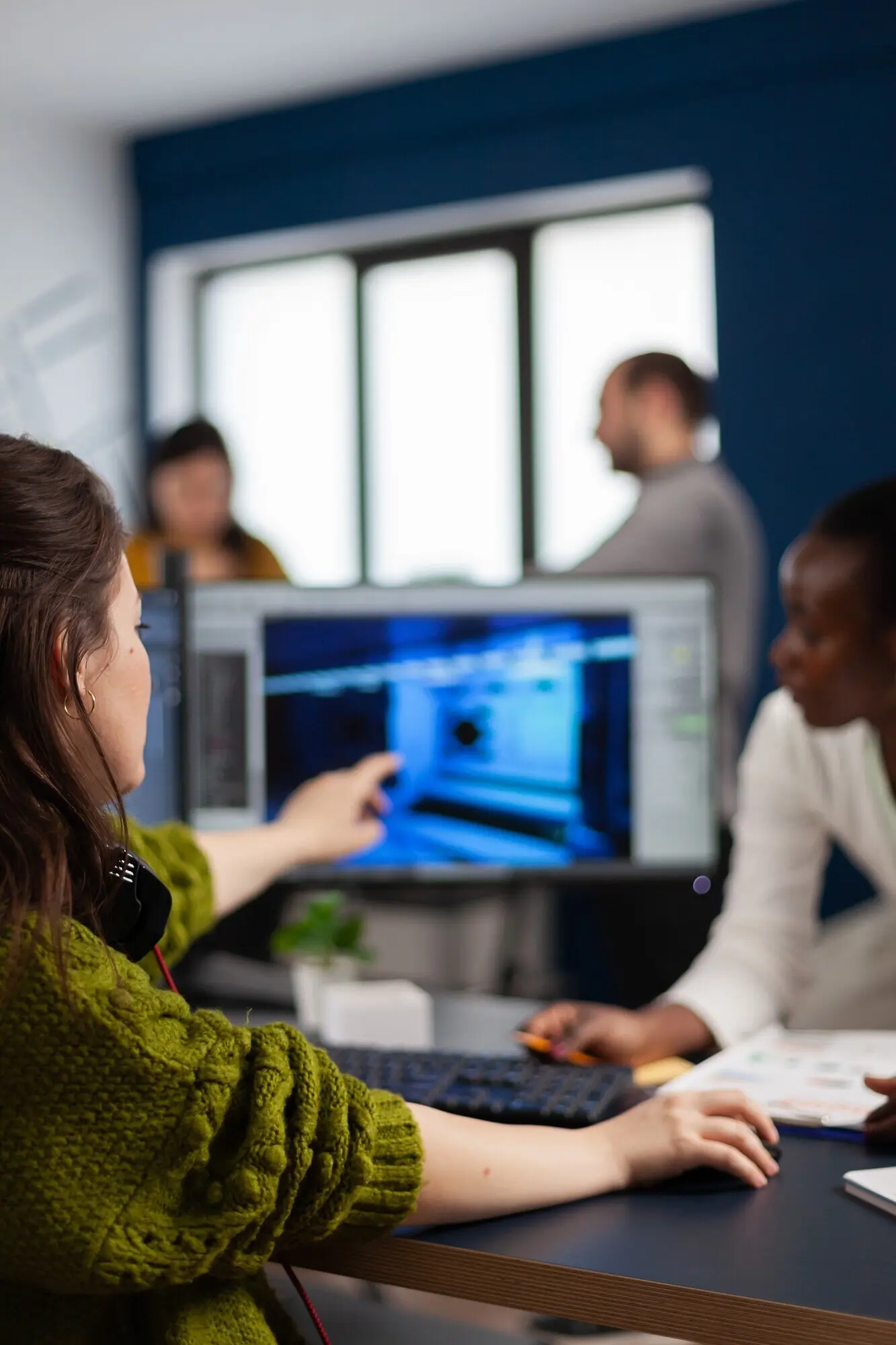 В креативном офисе создатель игр, указывая на экран, объясняет африканскому сотруднику, как тестировать интерфейс уровня игры при разработке нового дизайна.