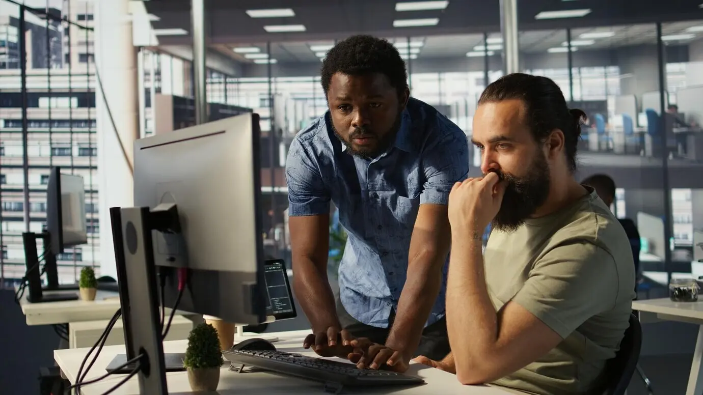 Сотрудник использует компьютер для анализа наборов данных при помощи коллеги.